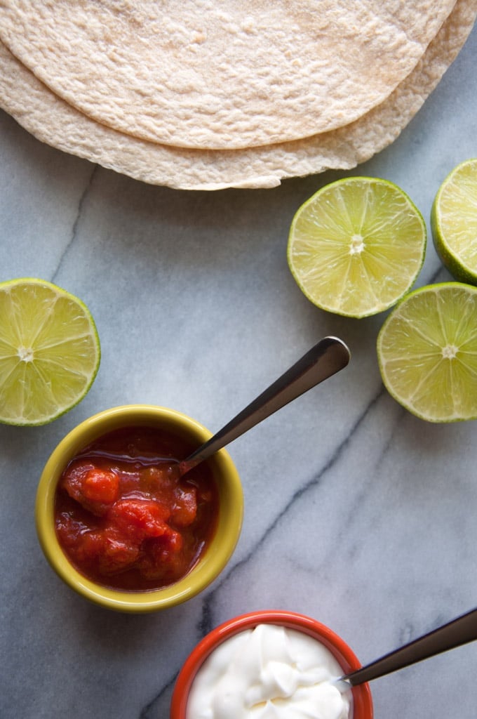 tortillas, limes, and a small bowl of salsa on a marble surface