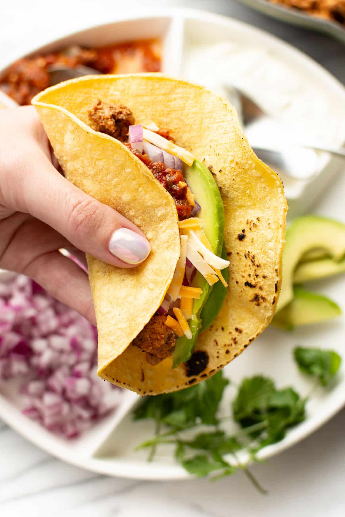 a female hand holding a ground turkey taco next to a dish with toppings