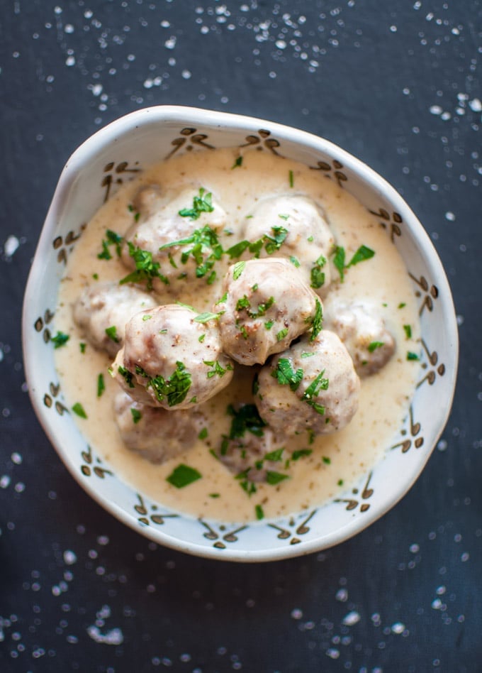 white bowl with several beef meatballs in a creamy white wine Dijon sauce and parsley garnish