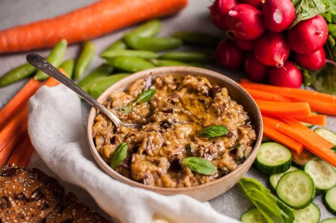 bowl with roasted eggplant dip and spoon next to veggies