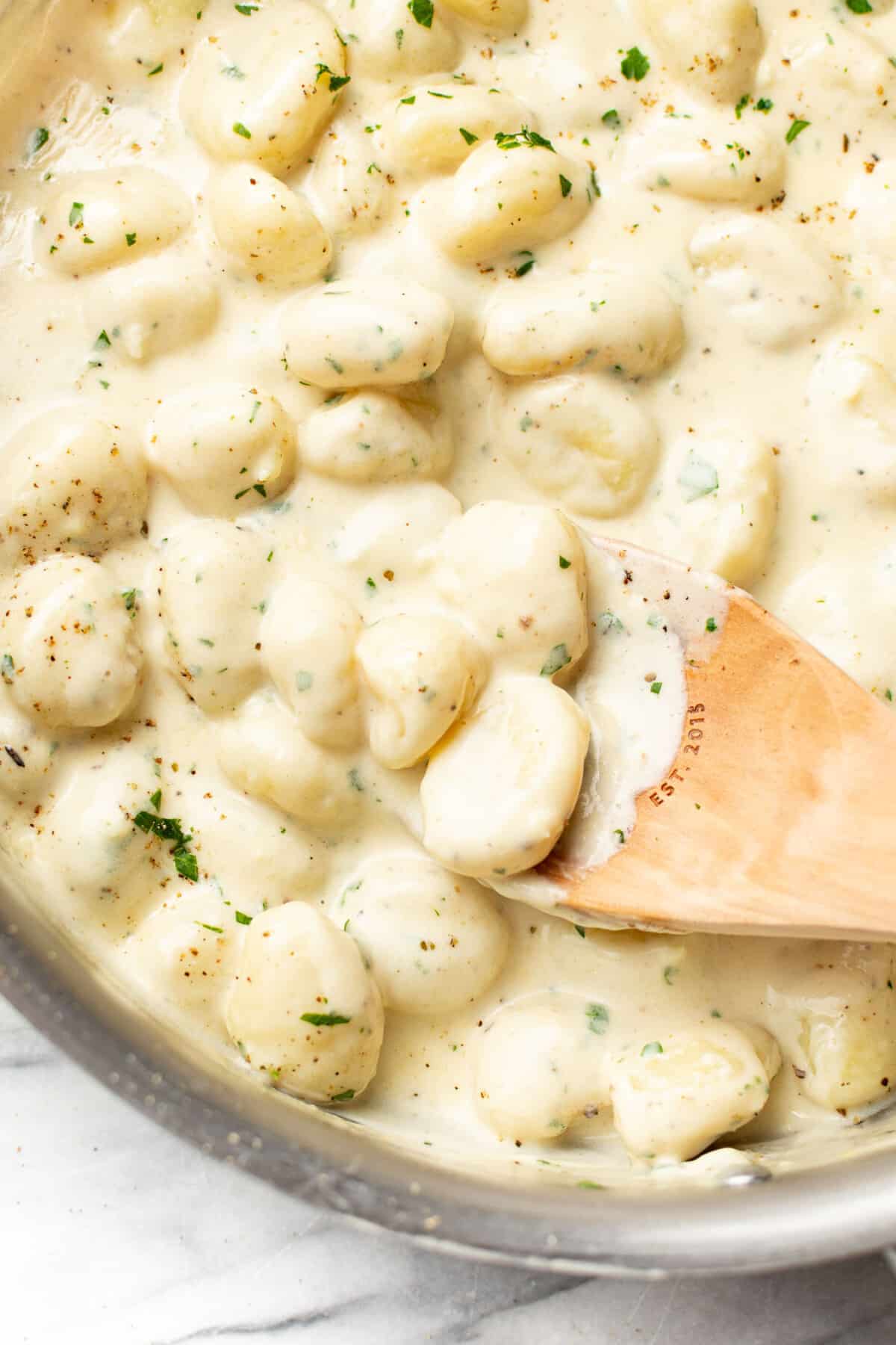 a skillet with creamy alfredo gnocchi and a wooden spoon