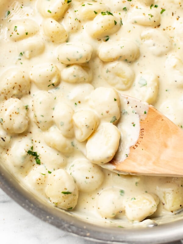 a skillet with creamy alfredo gnocchi and a wooden spoon