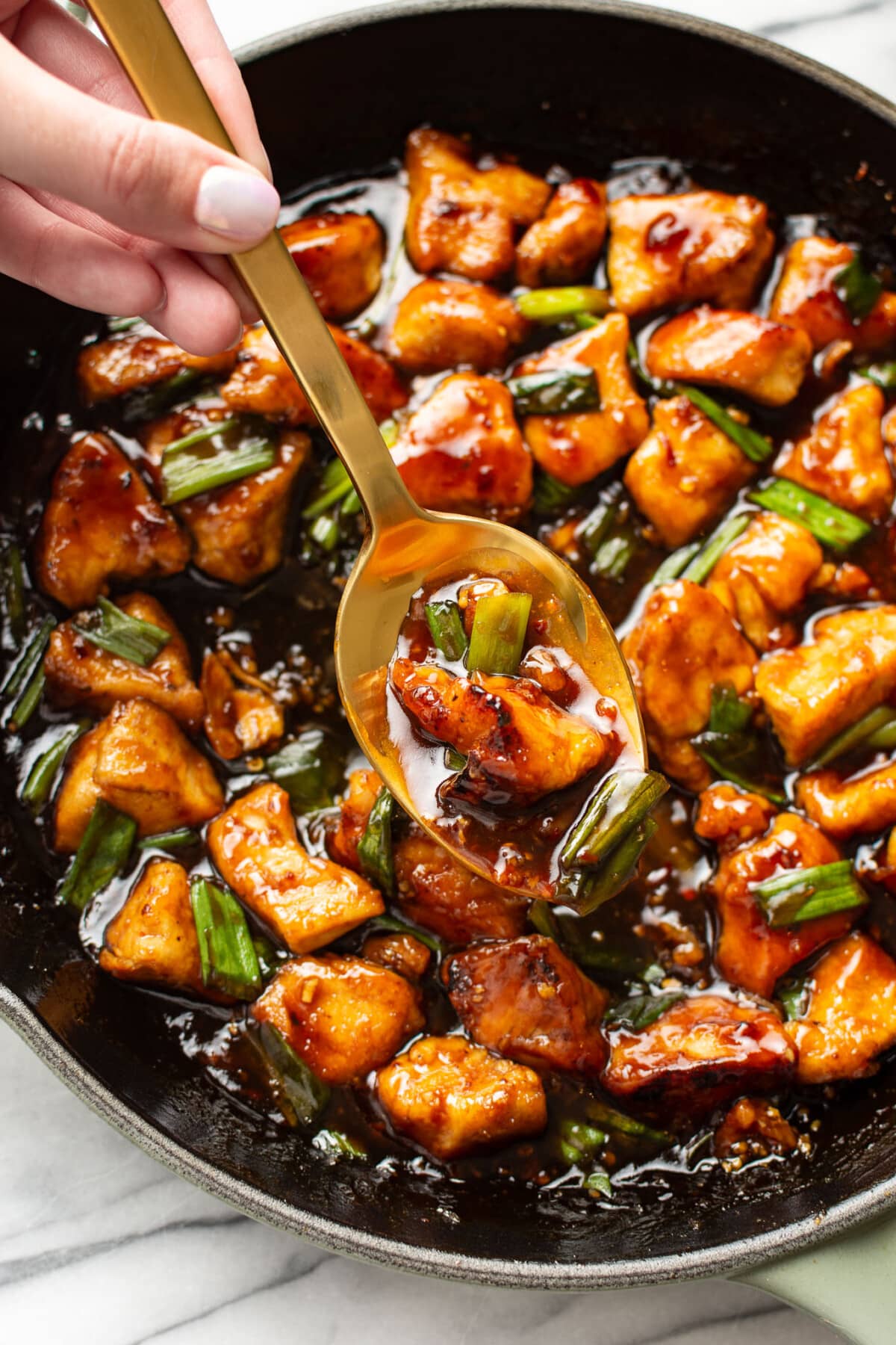 a female hand holding a serving spoon with mongolian chicken over a skillet
