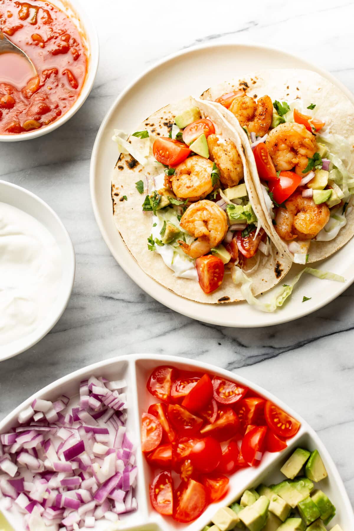 a plate with shrimp tacos next to fresh toppings