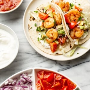 a plate with shrimp tacos next to fresh toppings