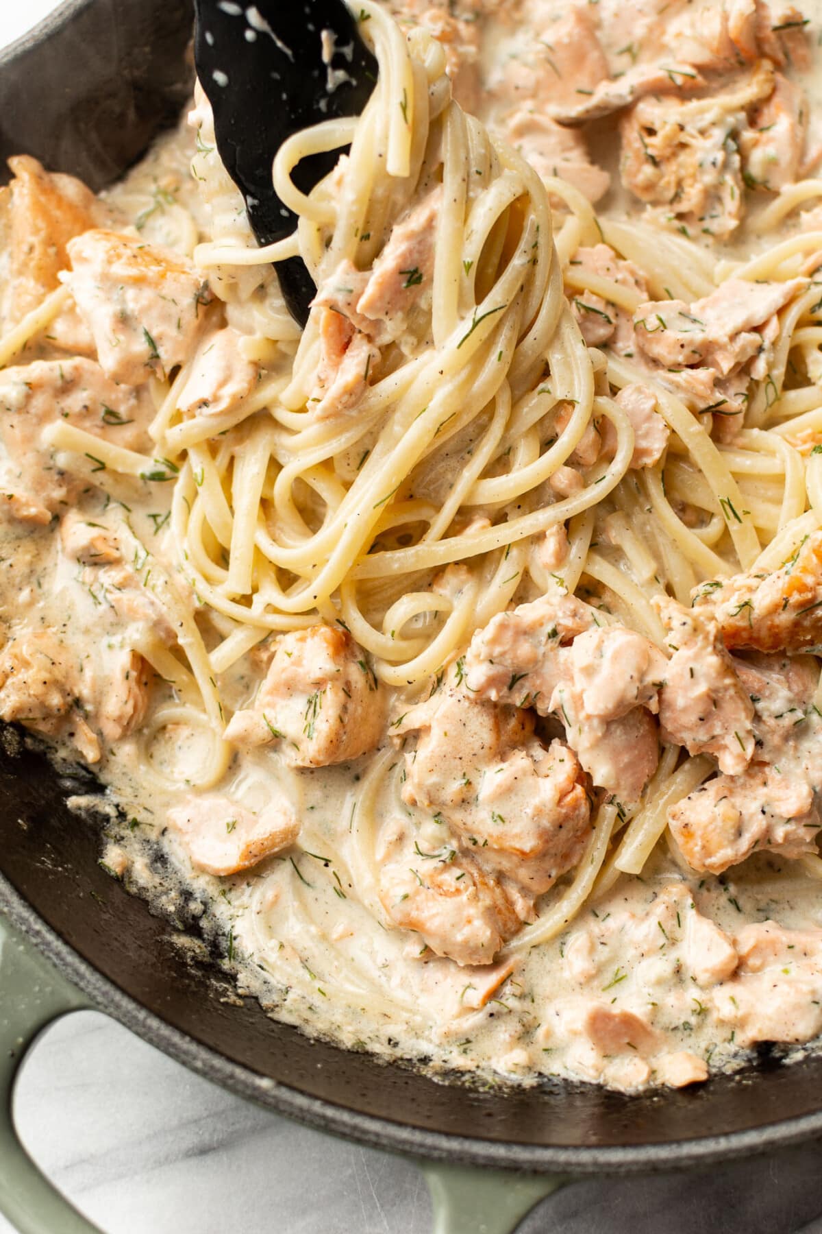 tossing creamy lemon dill salmon pasta in a skillet with cooking tongs