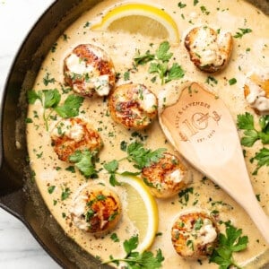 a skillet with creamy garlic lemon pan seared scallops and a wooden spoon