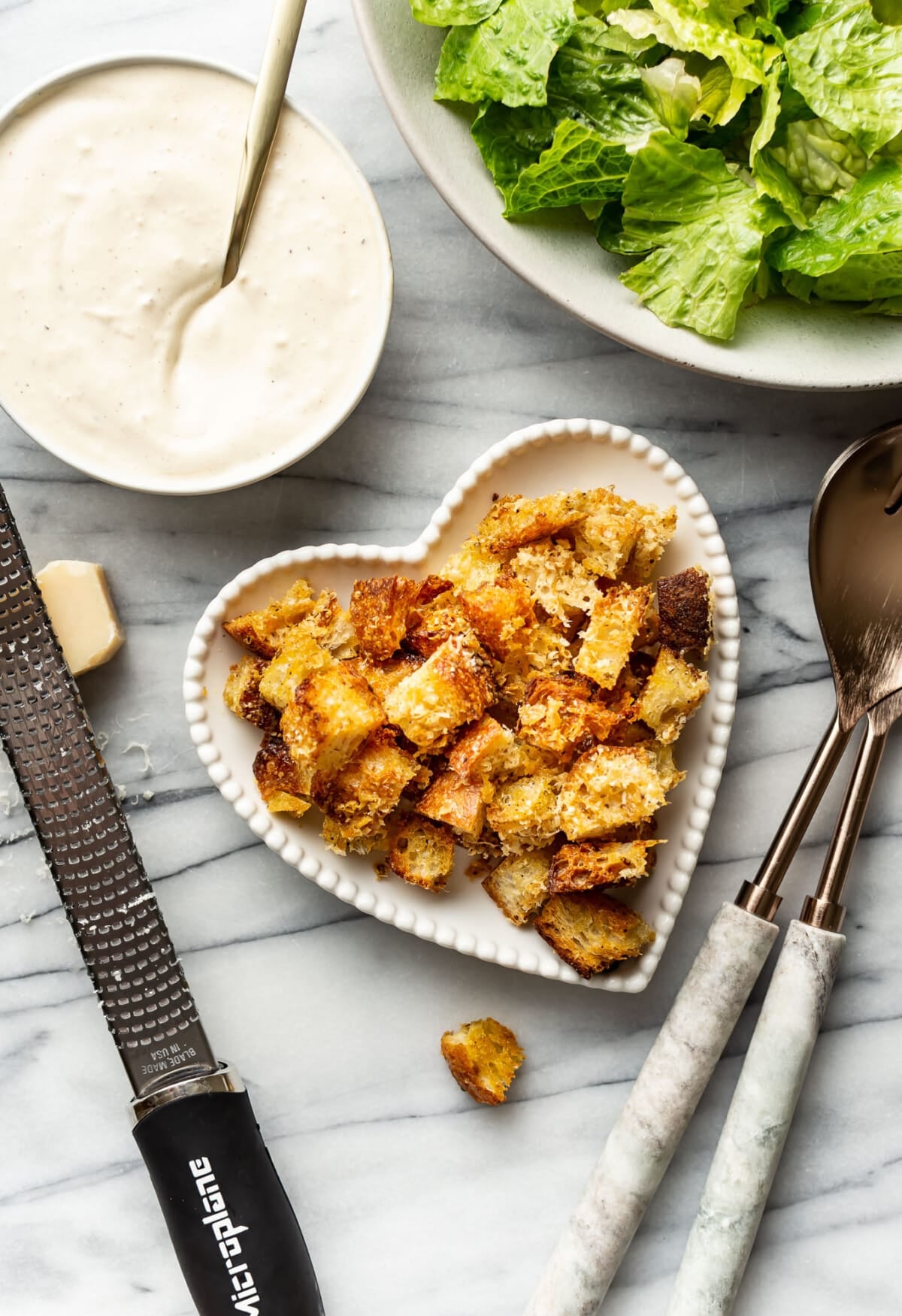 a bowl of croutons next to a salad and caesar dressing