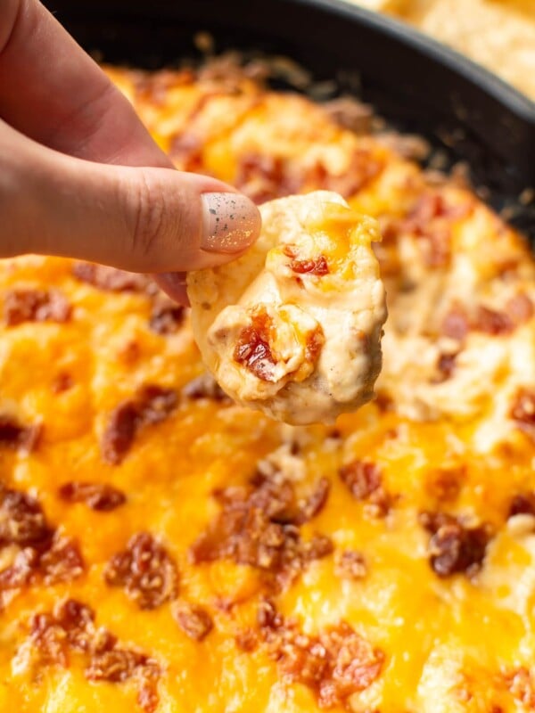 holding a chip scooping cheddar bacon dip from skillet