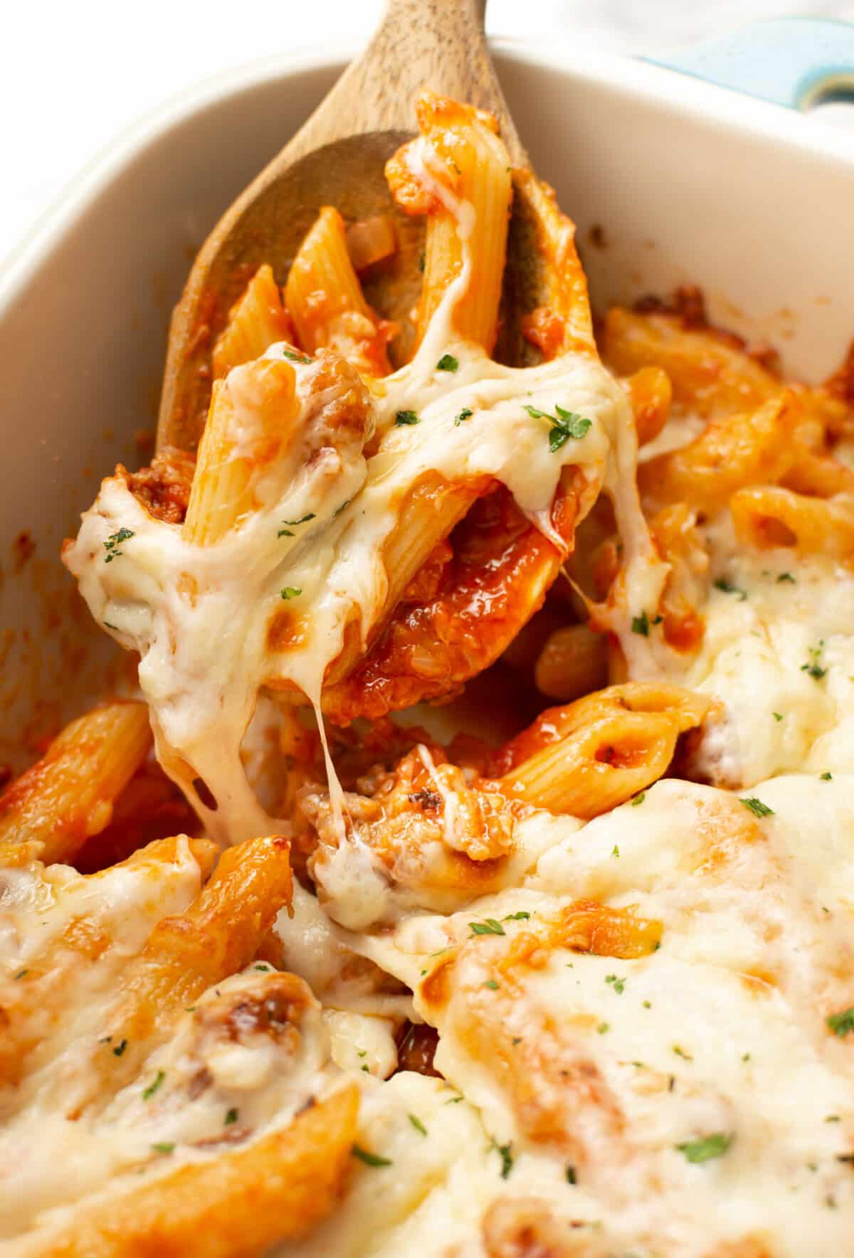 a casserole dish with baked penne with italian sausage and wooden serving spoon