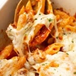 a casserole dish with baked penne with italian sausage and wooden serving spoon