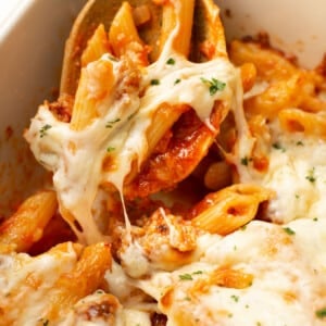 a casserole dish with baked penne with italian sausage and wooden serving spoon