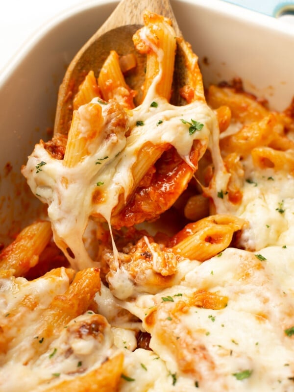 a casserole dish with baked penne with italian sausage and wooden serving spoon