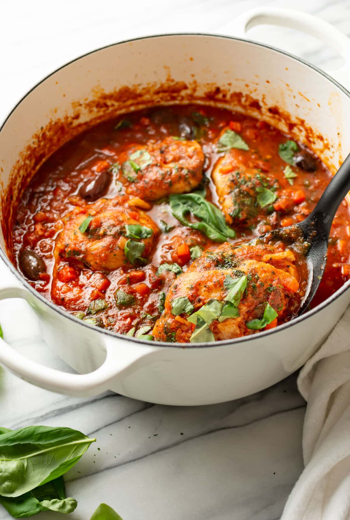 a dutch oven with chicken cacciatore and a serving spoon