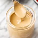 close-up of creamy balsamic dressing being drizzled from a spoon over a glass jar of dressing