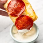 a hand dipping a slice of pepperoni french bread pizza in dip