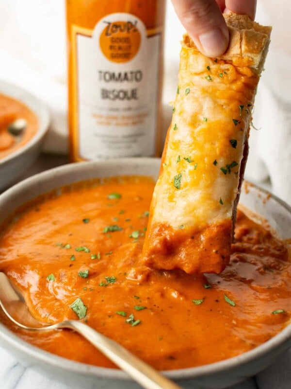 a piece of cheesy bread being dipped into zoup tomato bisque