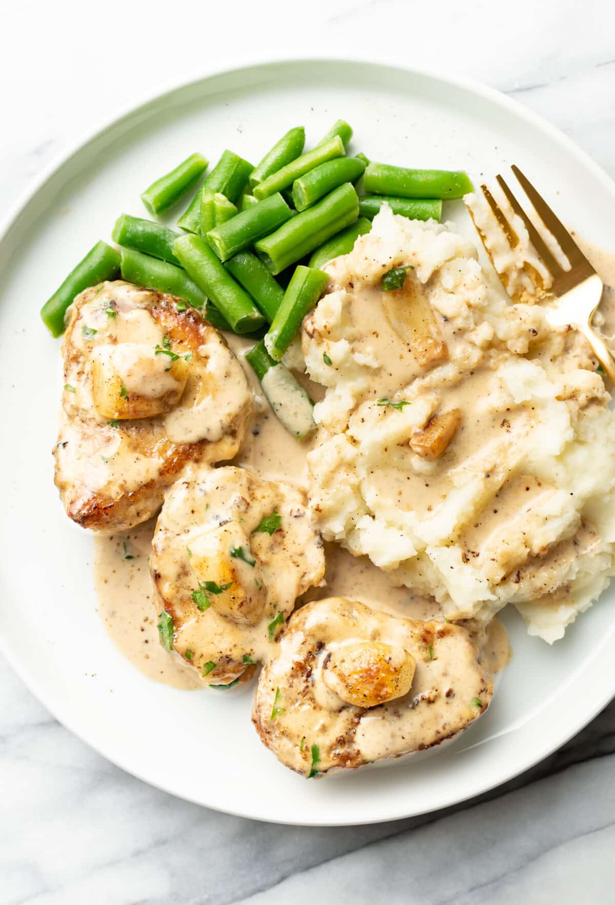 a plate with creamy garlic pork tenderloin, green beans, mashed potatoes, and a fork