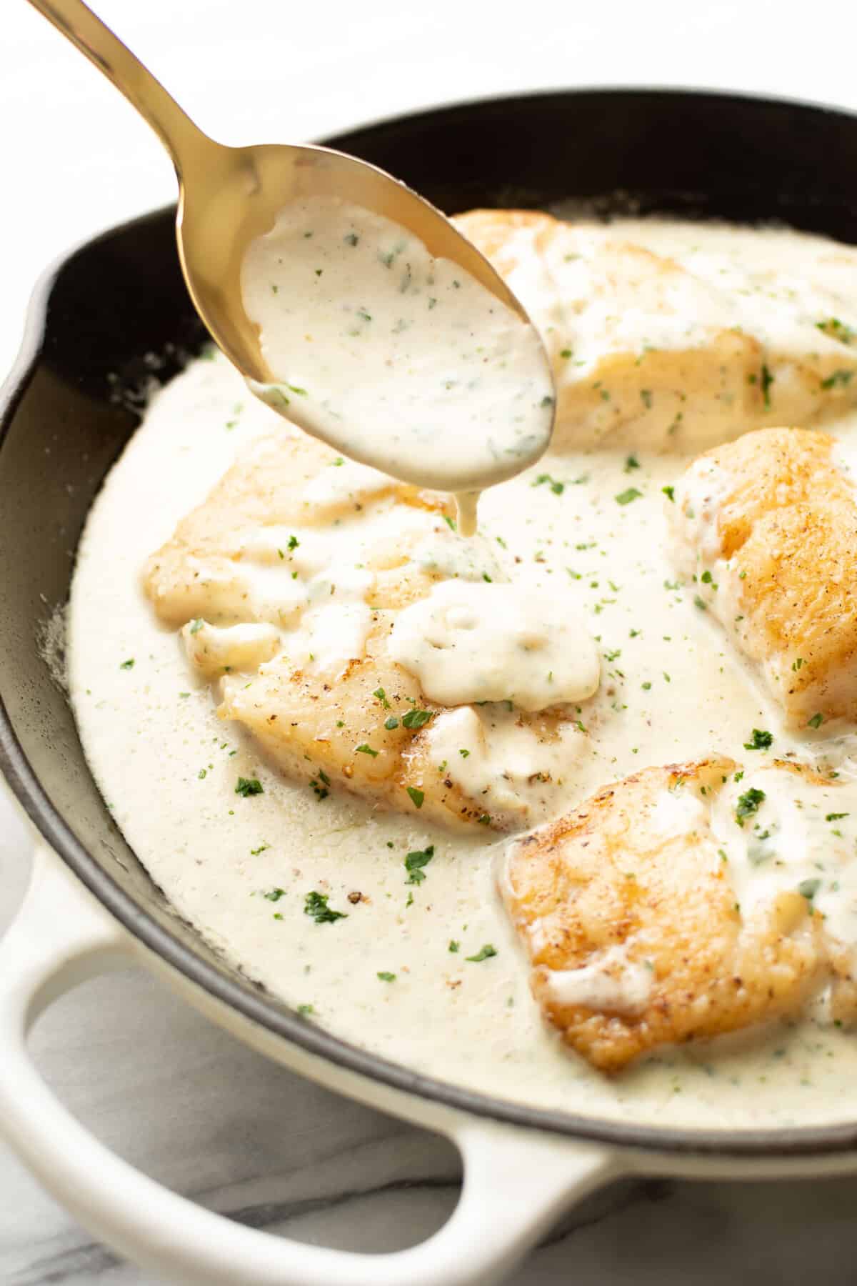 a skillet with creamy lemon parmesan cod and a serving spoon