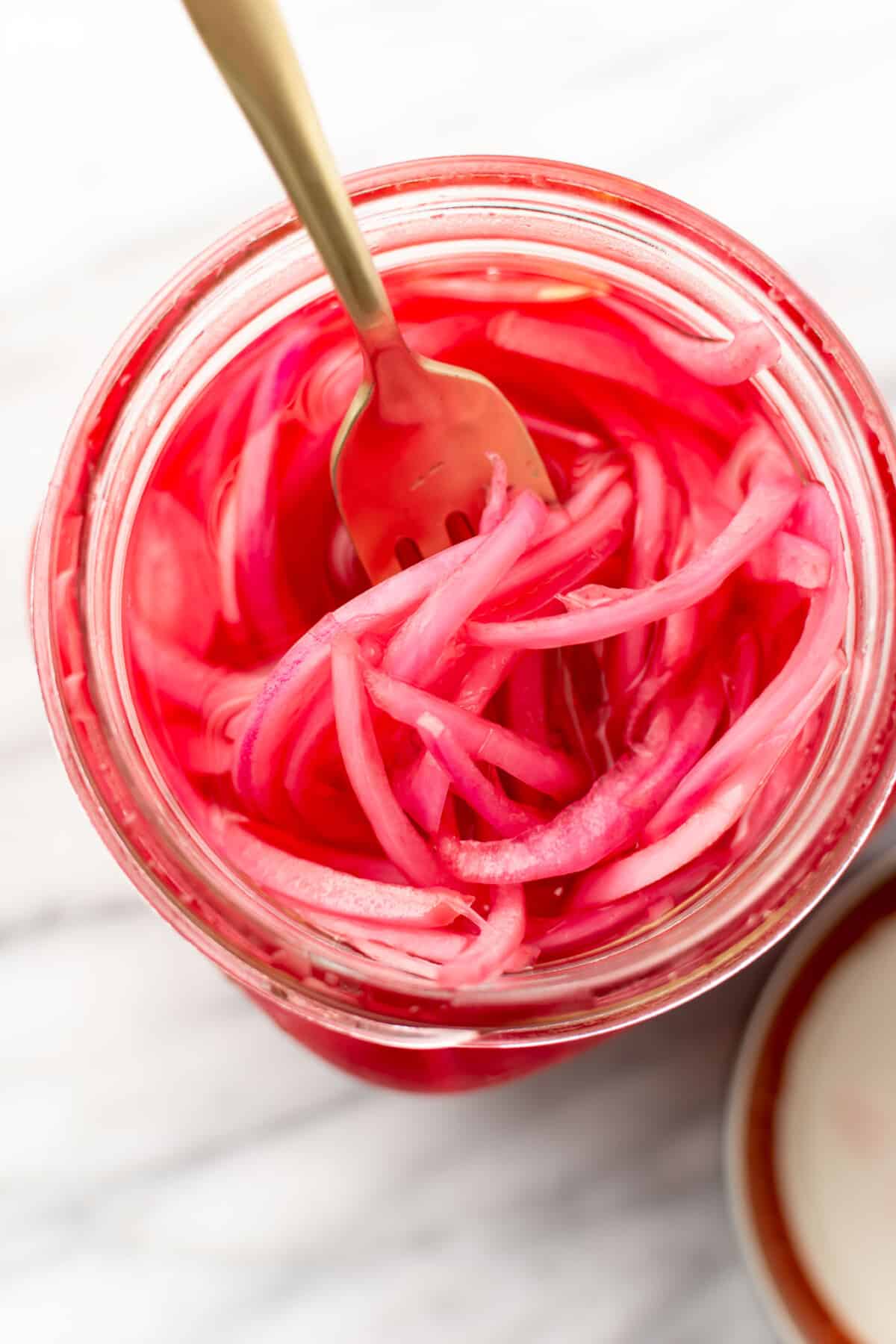 a jar of pickled red onions with a fork