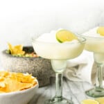two frozen margaritas next to a bowl of guacamole and chips