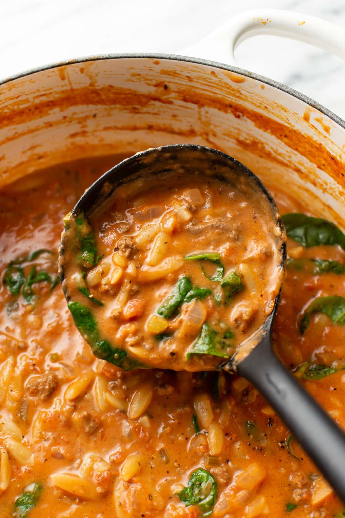 a dutch oven with ground beef orzo soup and a ladle
