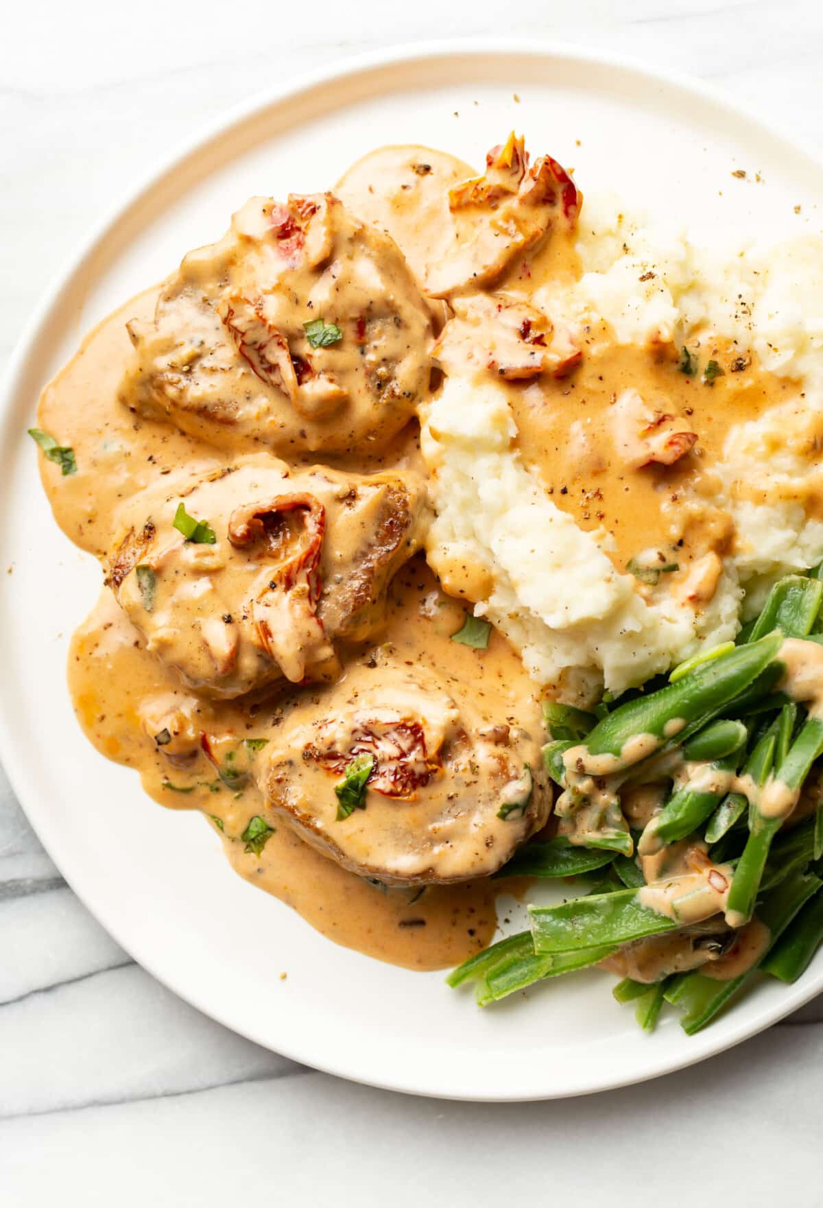 a plate with marry me pork tenderloin, mashed potatoes, and green beans