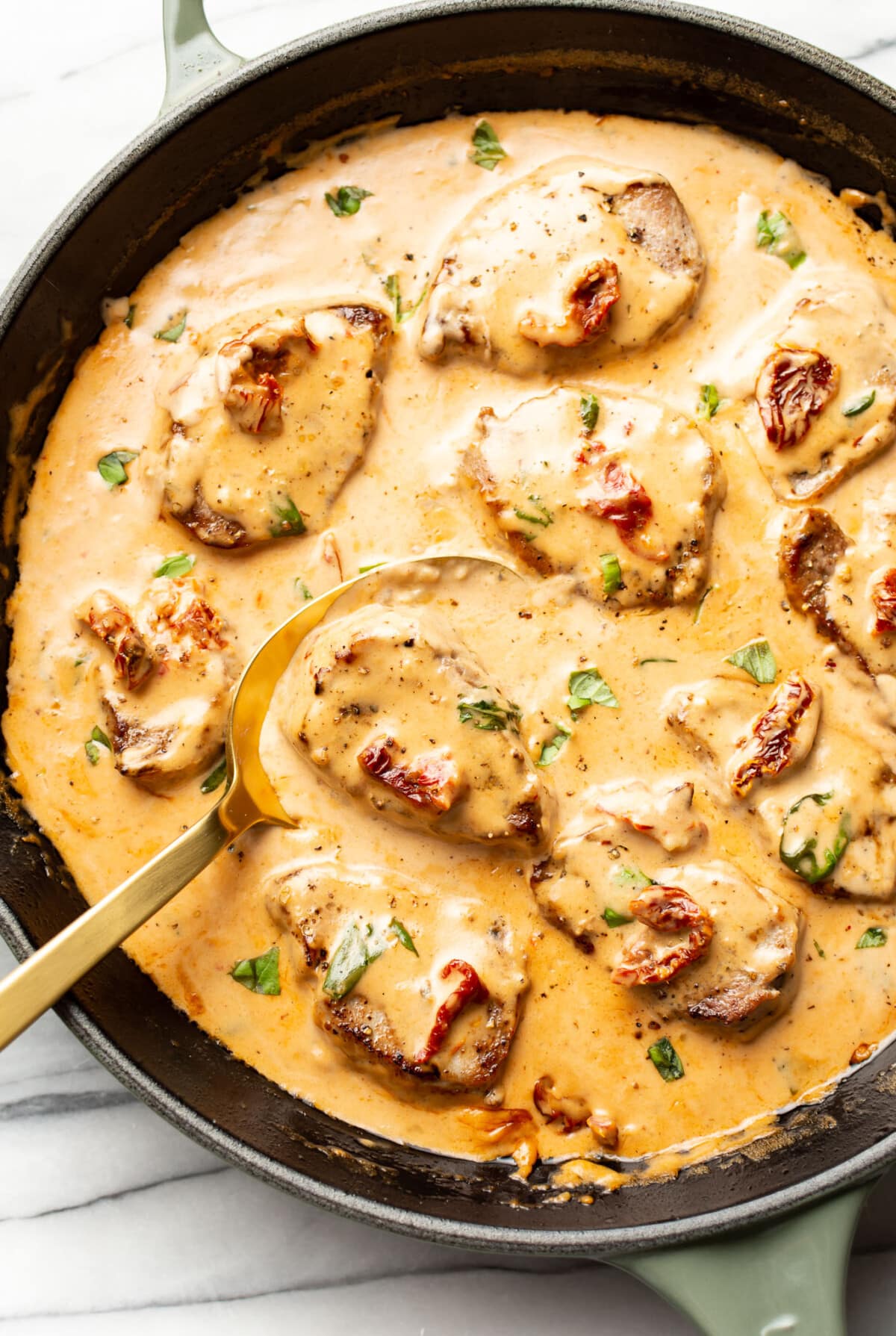 a skillet with marry me pork tenderloin and a serving spoon