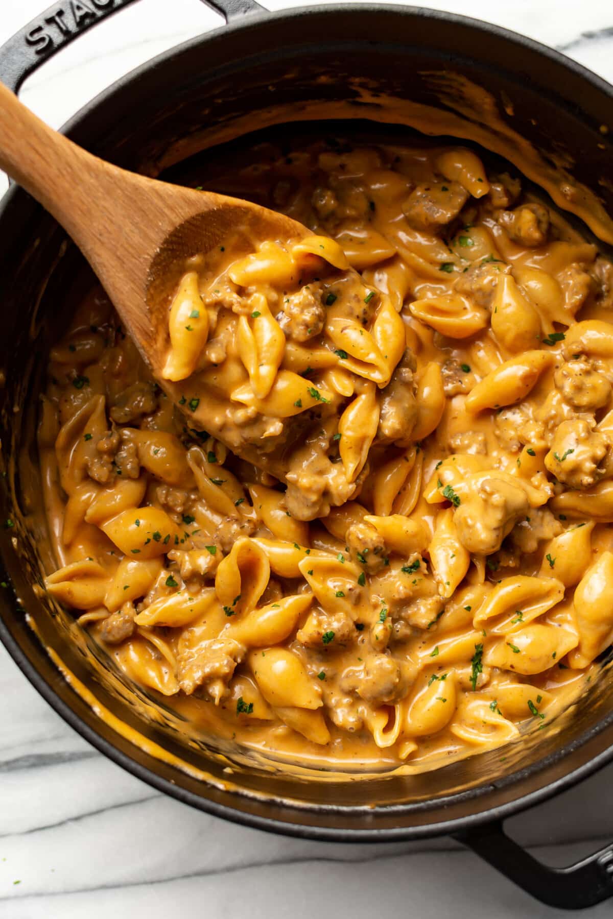 a pot with cheesy sausage and shells and a wooden spoon