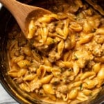 a pot with cheesy sausage and shells and a wooden spoon