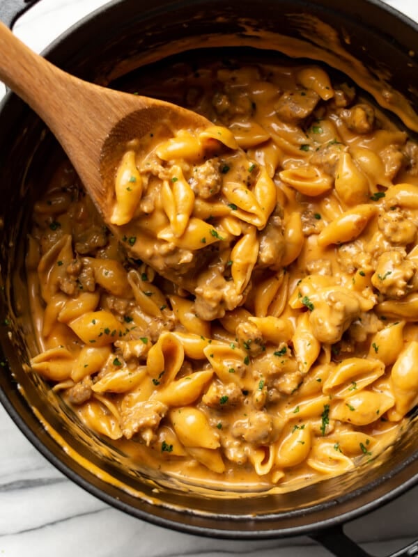 a pot with cheesy sausage and shells and a wooden spoon