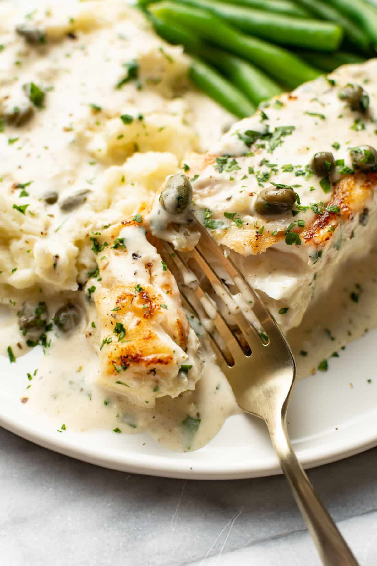 a plate with halibut, a creamy sauce, green beans, mashed potatoes, and a fork