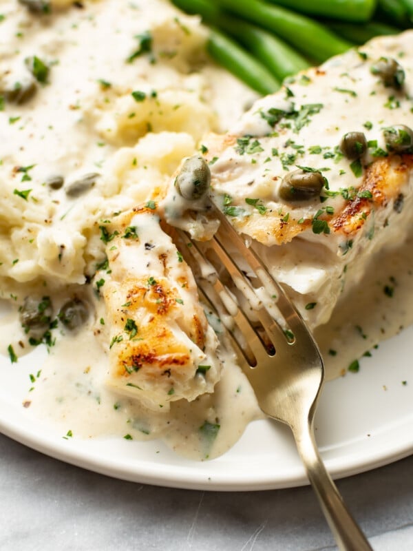 a plate with halibut, a creamy sauce, green beans, mashed potatoes, and a fork