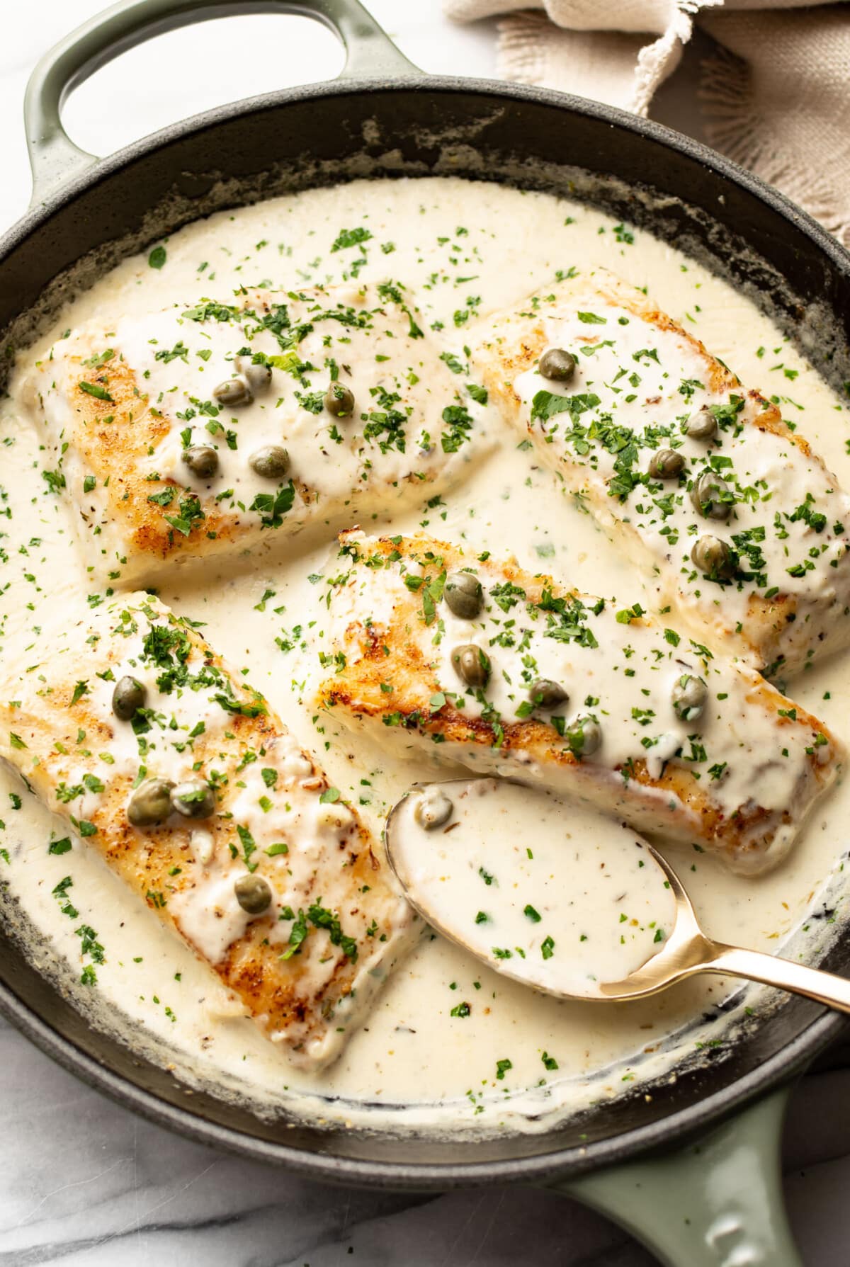 a skillet with creamy white wine halibut and a serving spoon
