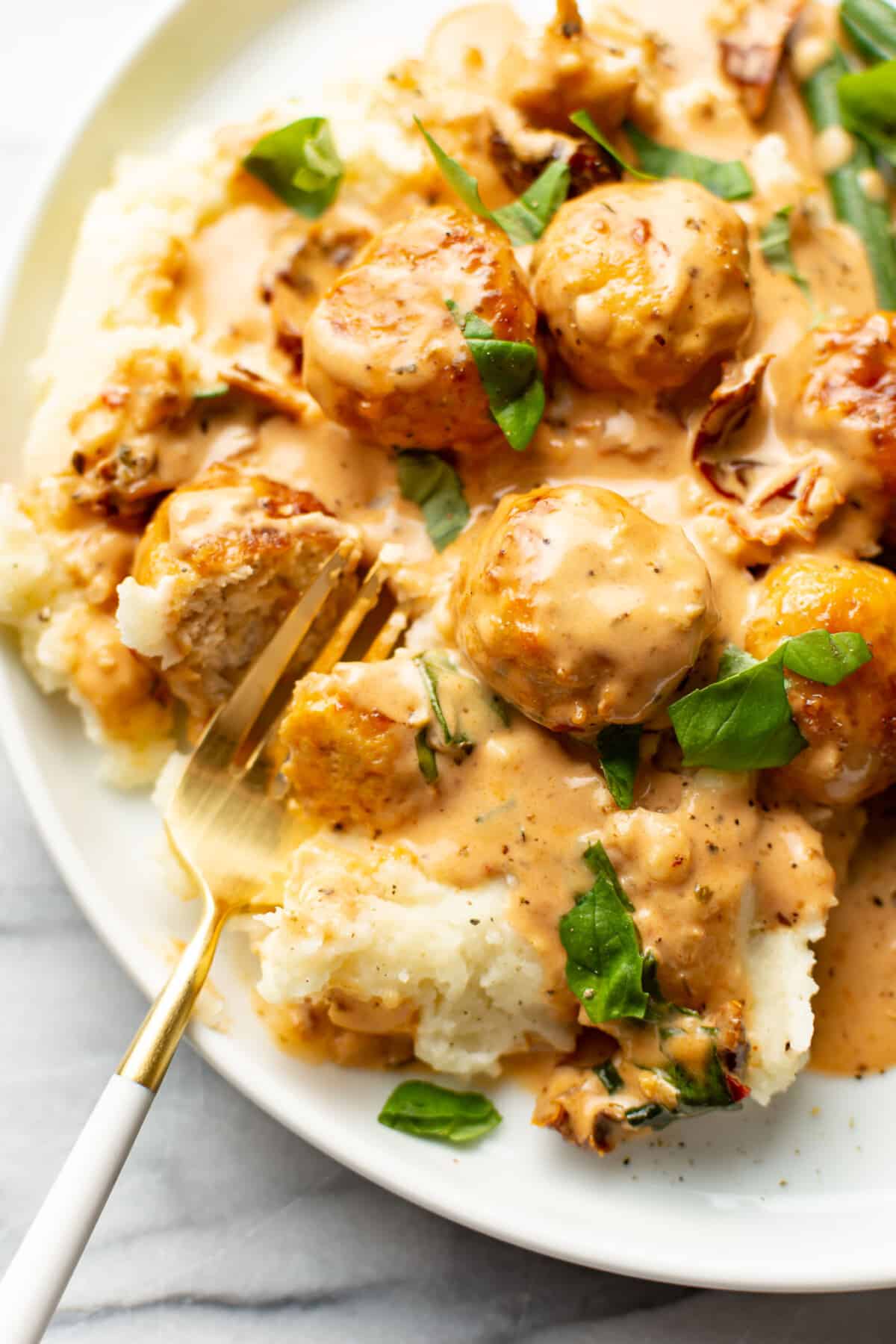 a plate with marry me chicken meatballs over mashed potatoes with a fork