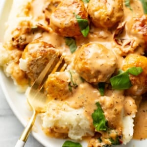 a plate with marry me chicken meatballs over mashed potatoes with a fork
