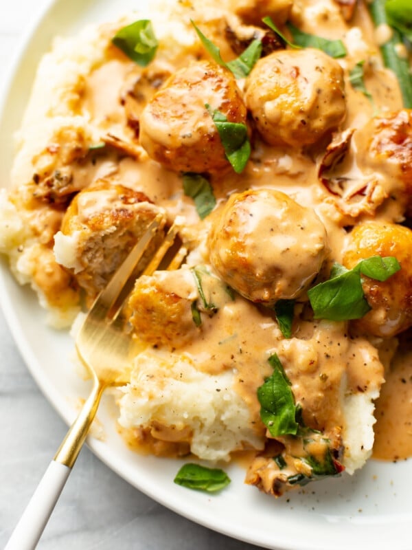 a plate with marry me chicken meatballs over mashed potatoes with a fork