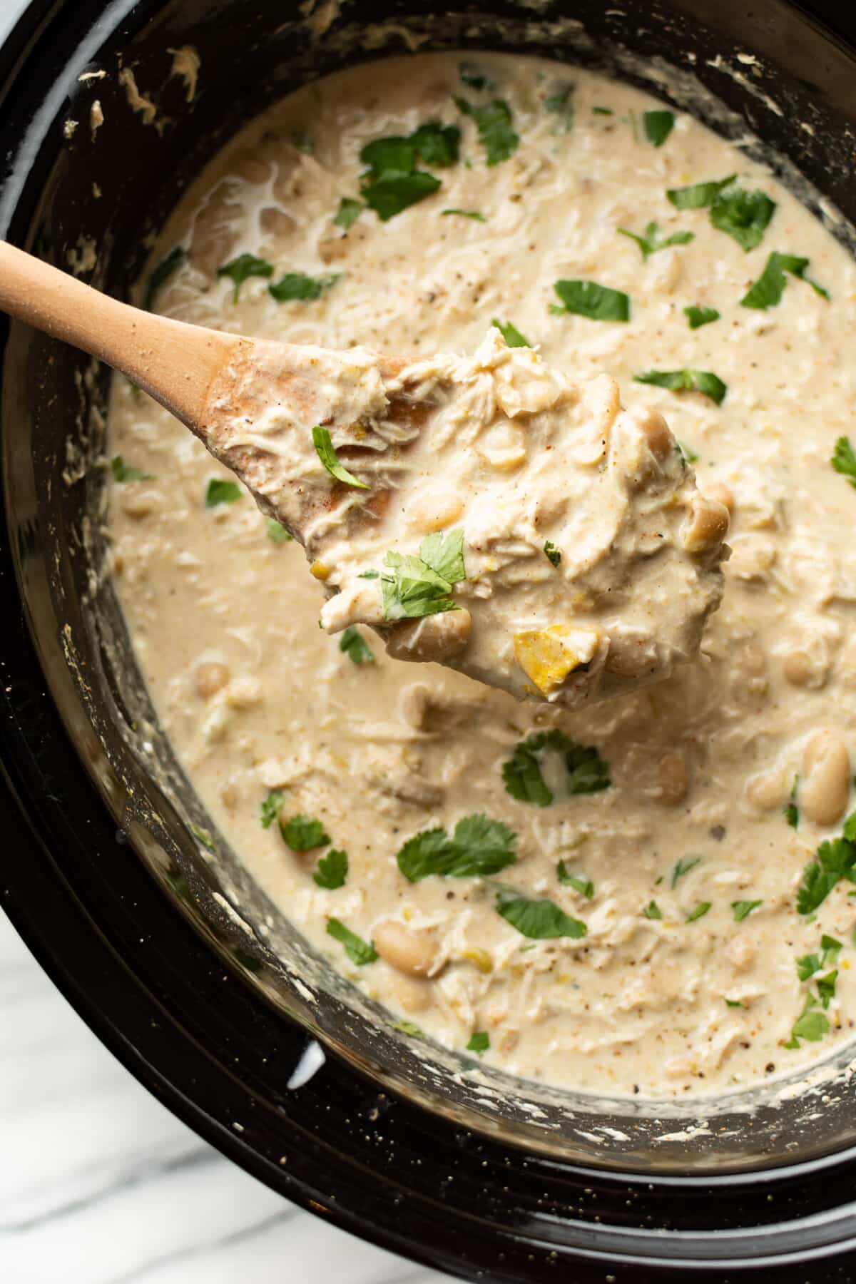 a crockpot with white chicken chili and a serving spoon