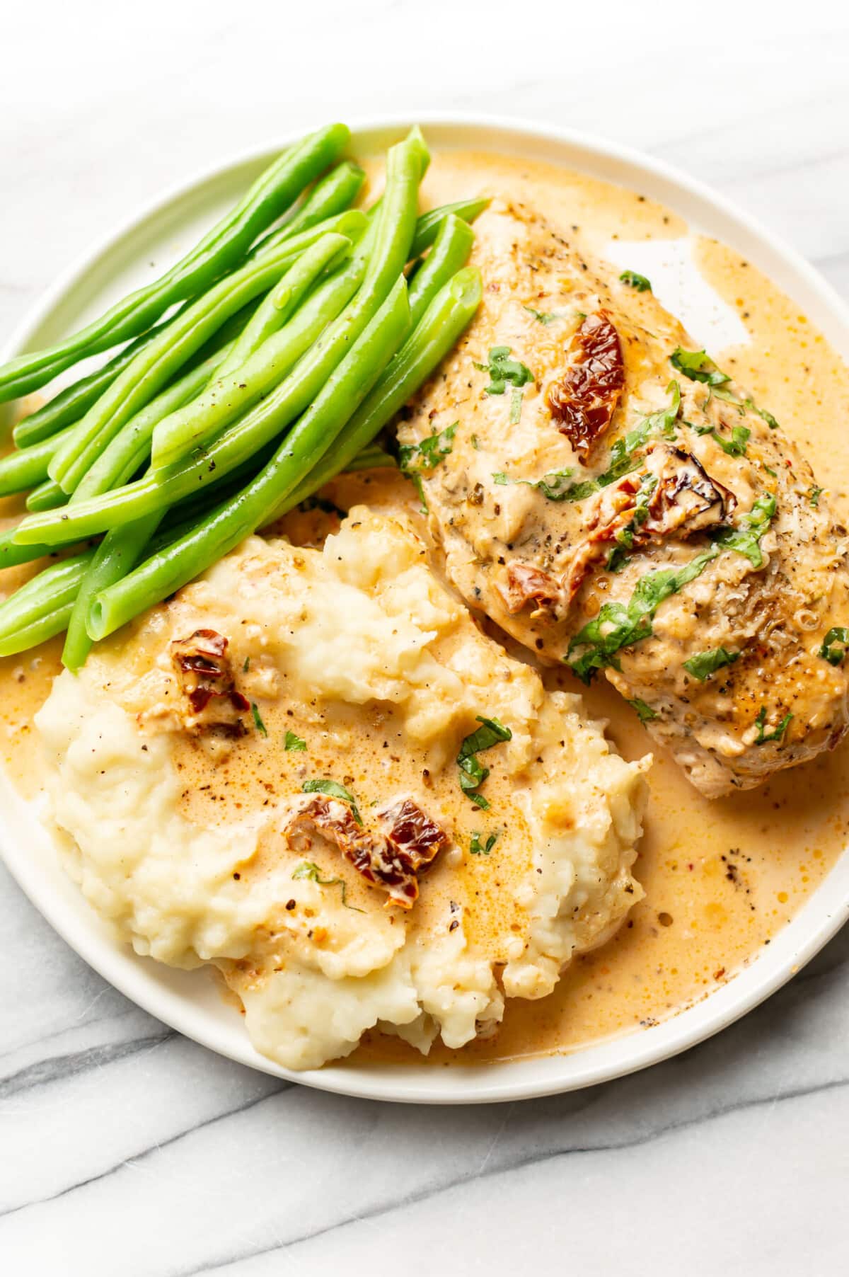 a plate with baked marry me chicken, green beans, and mashed potatoes