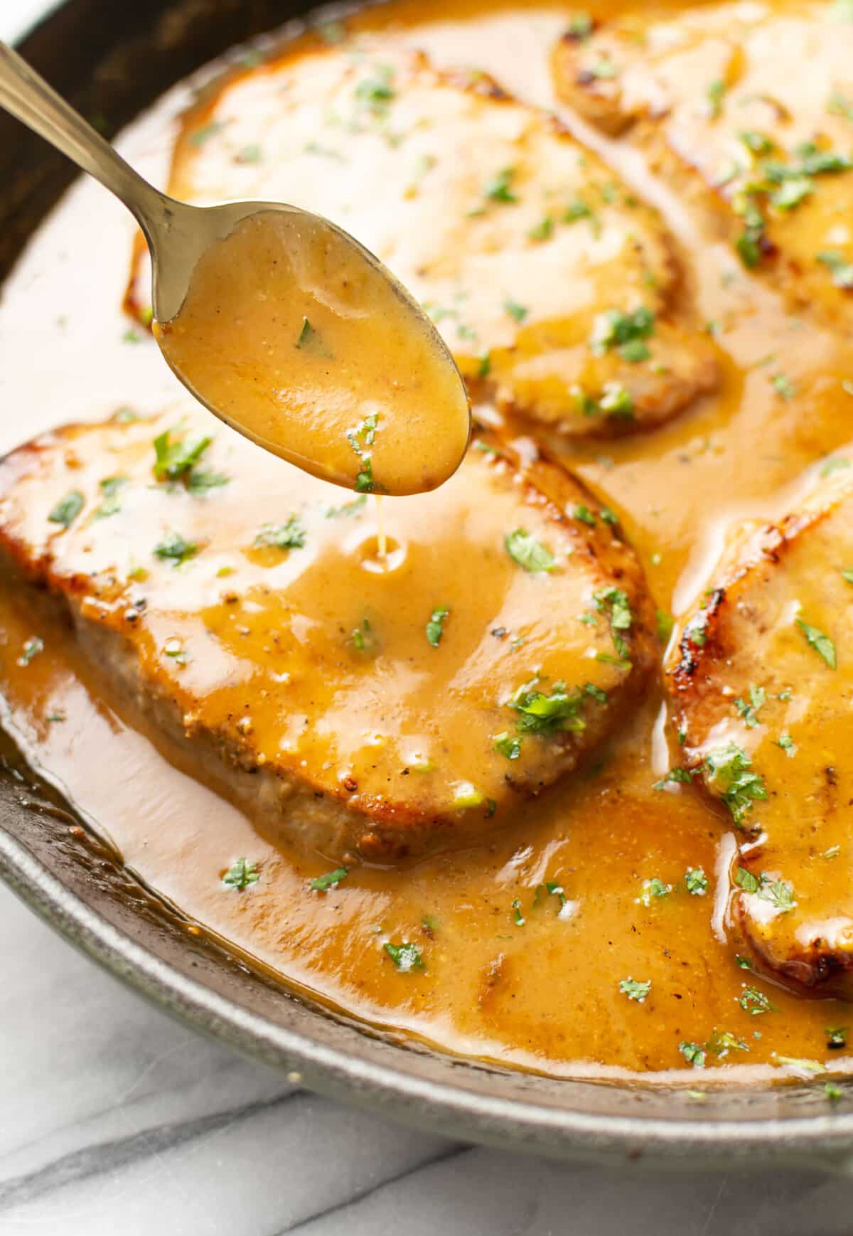 a skillet with honey mustard pork chops and a serving spoon