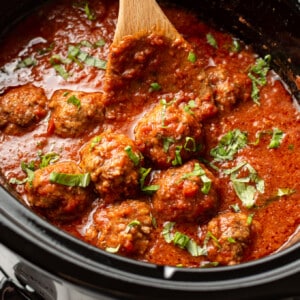 a crockpot with meatballs in tomato sauce with a wooden spoon