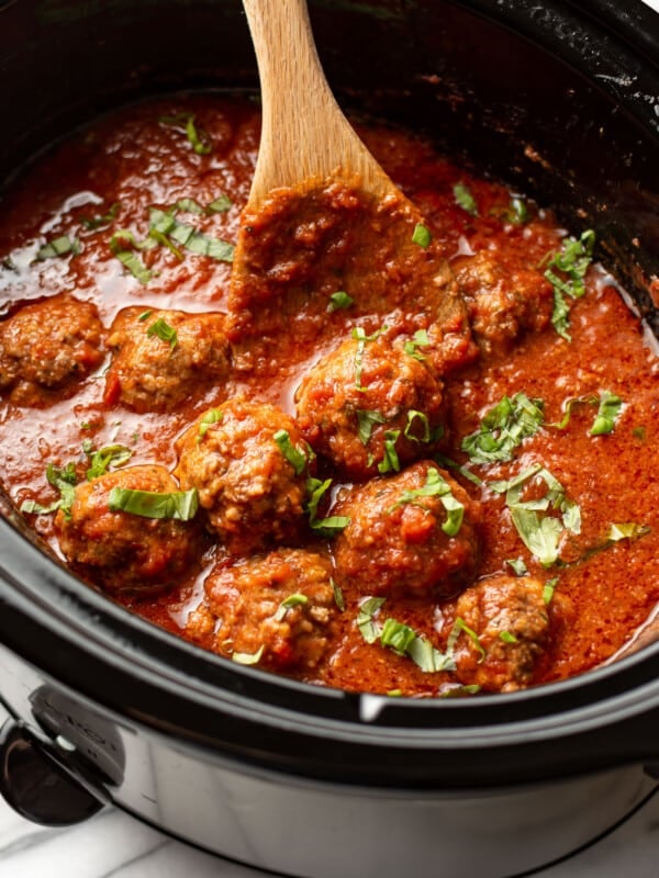 a crockpot with meatballs in tomato sauce with a wooden spoon