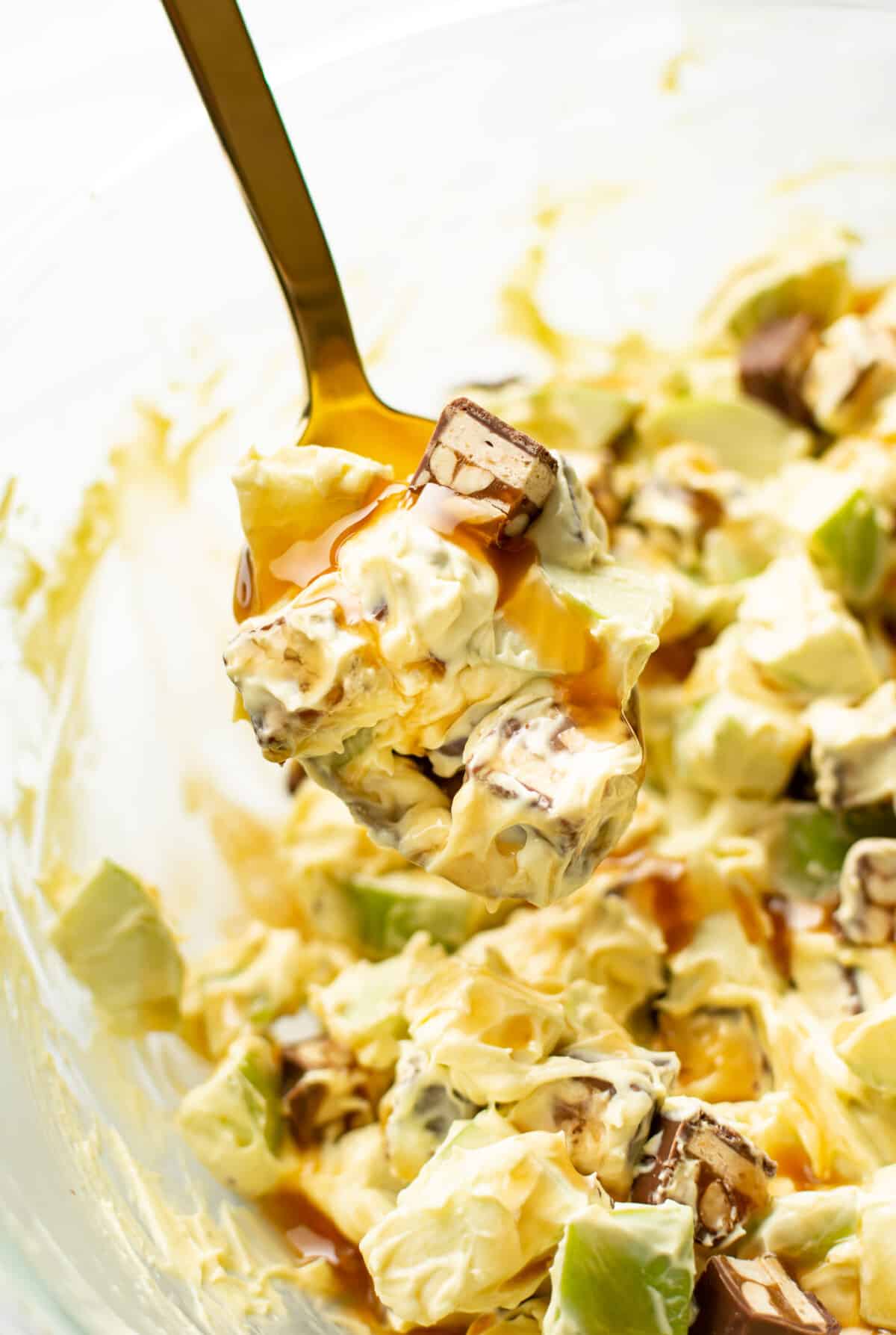 a bowl of snickers apple salad with a serving spoon