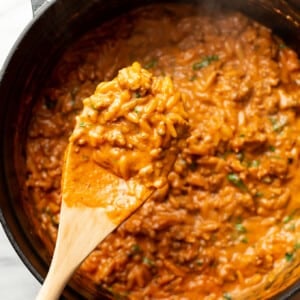 a pot of spicy italian sausage orzo with a wooden spoon