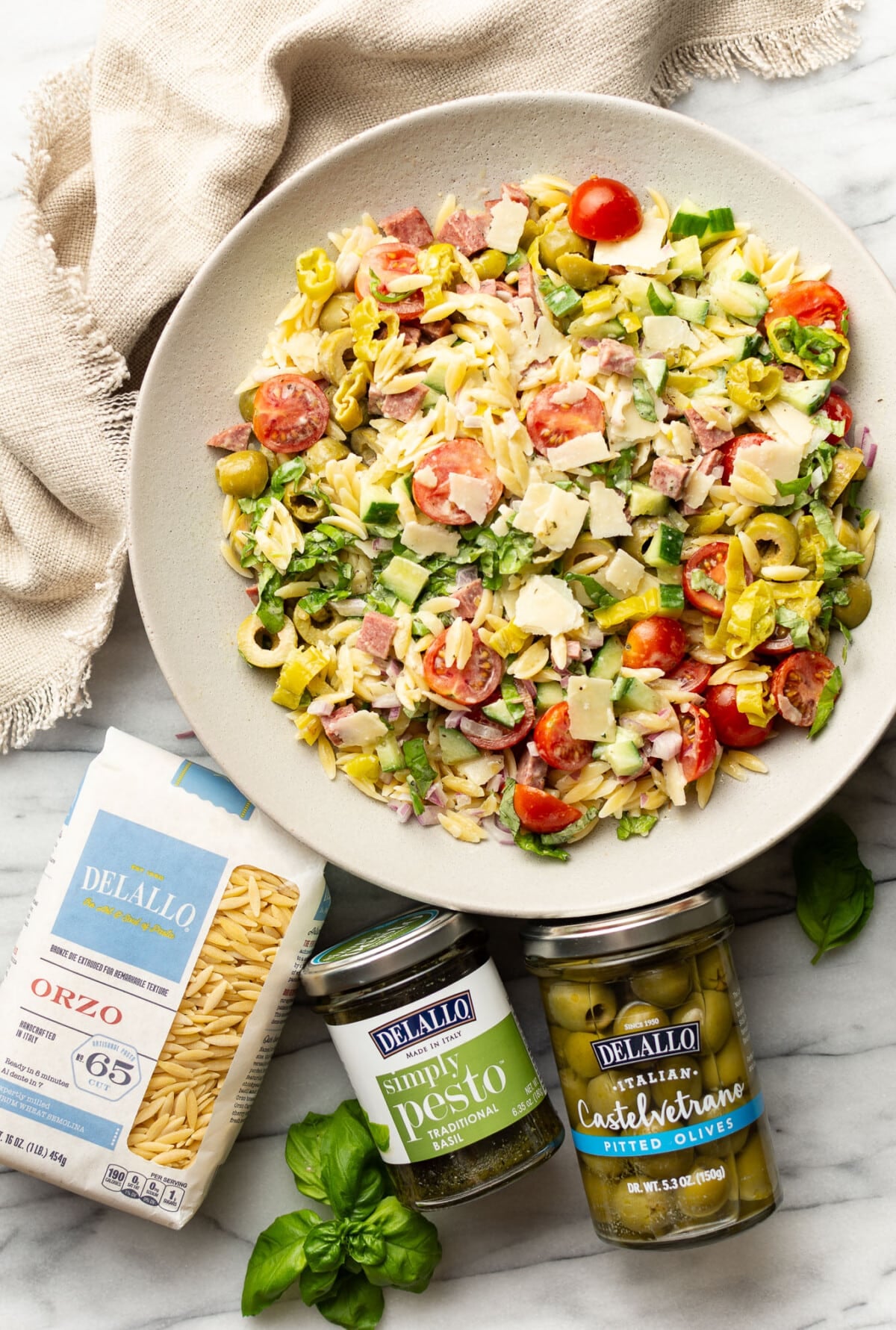 a bowl of italian orzo salad next to olives and other ingredients