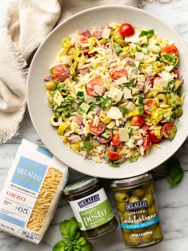 a bowl of italian orzo salad next to olives and other ingredients