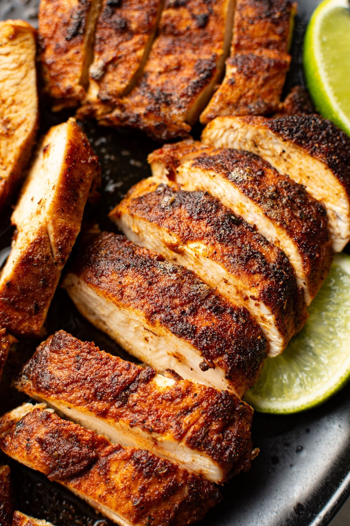 sliced blackened chicken on a plate next to lime wedges