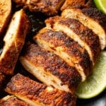 sliced blackened chicken on a plate next to lime wedges