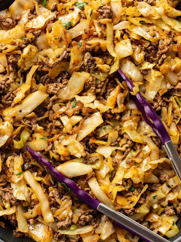 a skillet with ground beef and cabbage with kitchen tongs