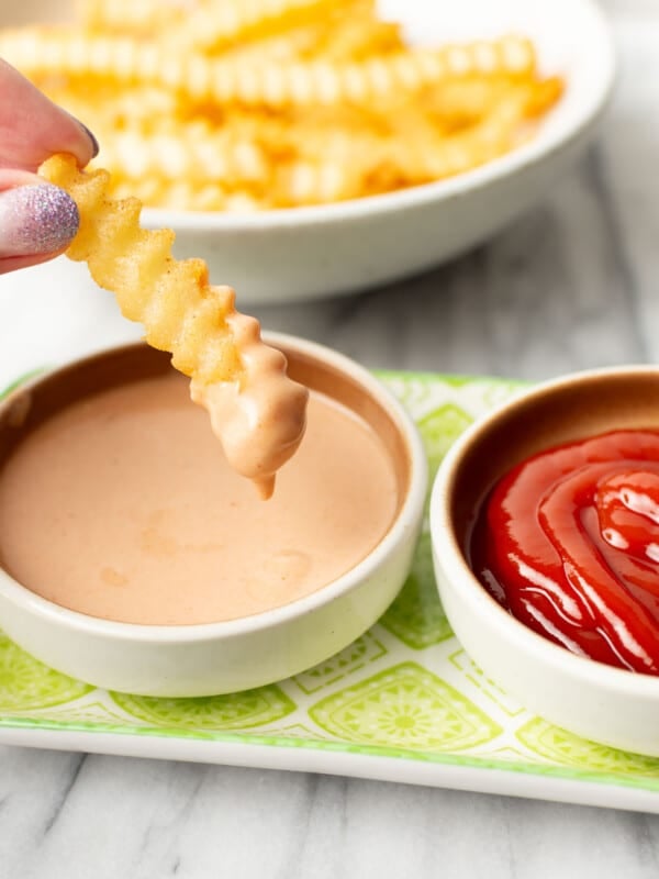 a female hand dipping a french fry into homemade fry sauce